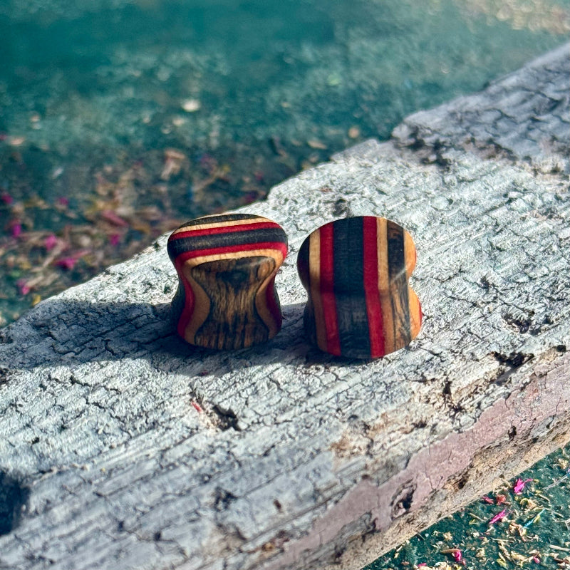 Red and Black Double Flare Wooden Ear Plugs 10mm with striped wood grain pattern on weathered surface outdoors