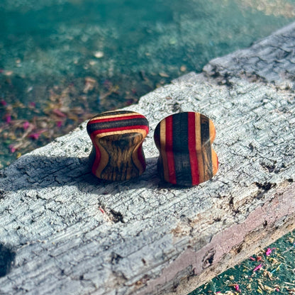 Red and Black Double Flare Wooden Ear Plugs 10mm with striped wood grain pattern on weathered surface outdoors