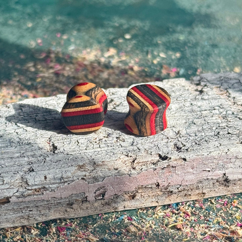 Red and Black Double Flare Wooden Ear Plugs 10mm with layered wood grain pattern on a textured surface outdoors