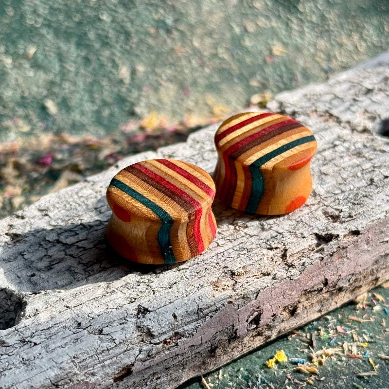 Red and brown 16mm ear plugs close up, red, yellow and blue layers through the maple.