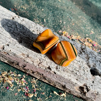 Green and yellow 16mm ear plugs on weathered wood, colour grain visible around the wall.