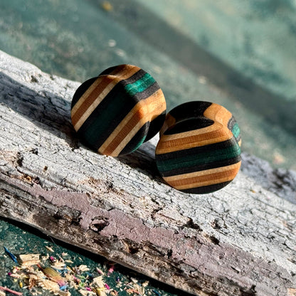 Teal and Black Double Flare Wooden Ear Plugs 16mm with striped wood pattern resting on textured bark surface
