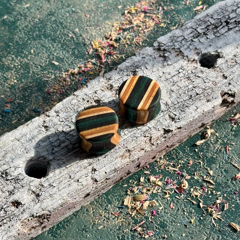 Teal and Black Double Flare Wooden Ear Plugs 16mm with striped wood pattern on textured rustic surface outdoors