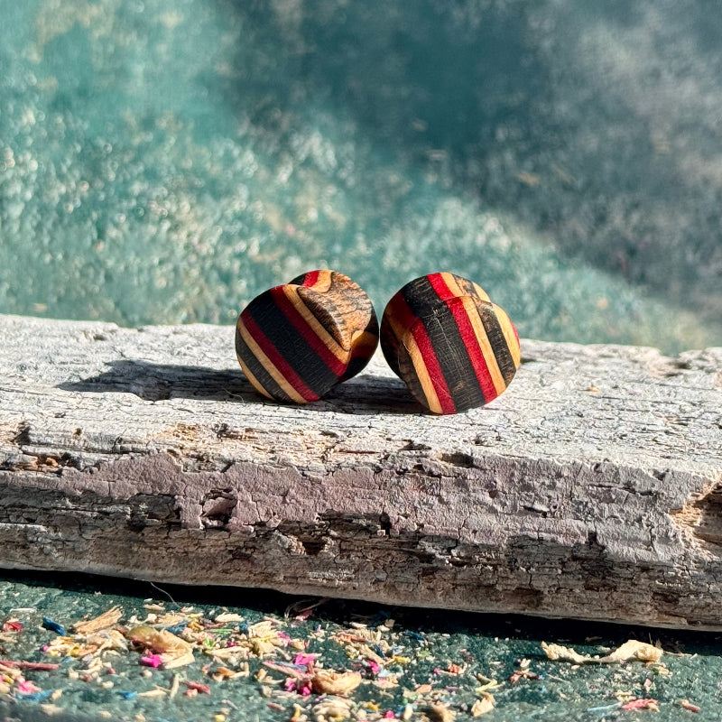 Red and Black Double Flare Wooden Ear Plugs 10mm resting on weathered driftwood with textured blue background
