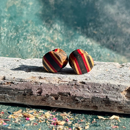 Red and Black Double Flare Wooden Ear Plugs 10mm resting on weathered driftwood with textured blue background