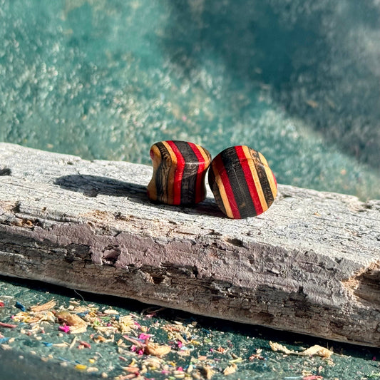 Red and Black Double Flare Wooden Ear Plugs 10mm with striped pattern on textured wooden surface outdoors