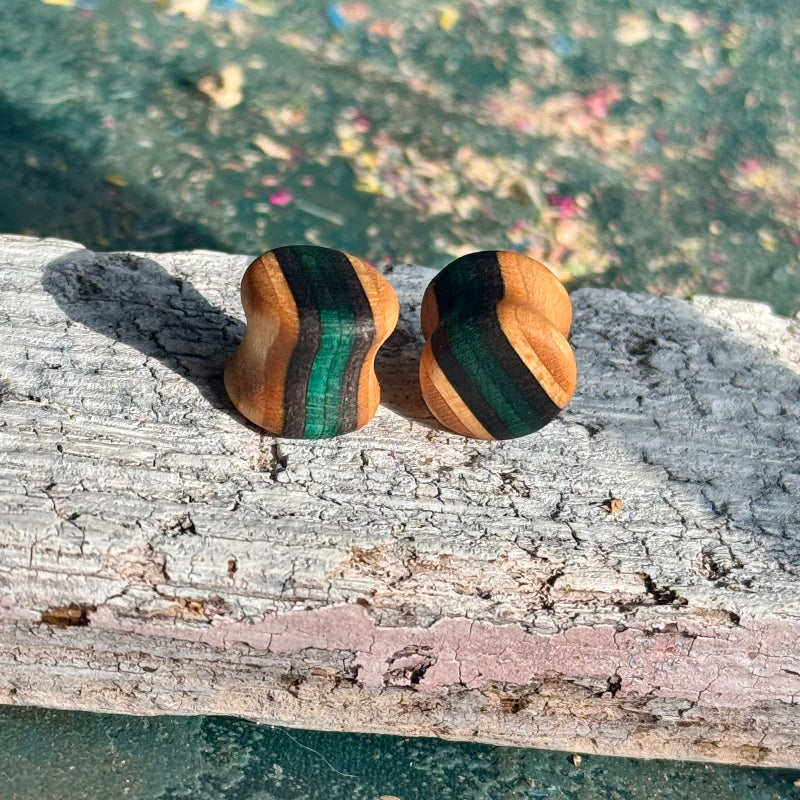 Teal and black 10mm ear plugs seen from the side, showing the double flare curve and natural grain.
