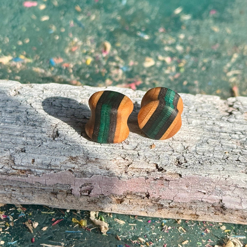 Teal and black double flare ear plugs at 10mm, layered skateboard maple stripes running through the wall.