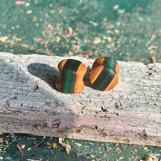 Teal and black double flare ear plugs at 10mm, layered skateboard maple stripes running through the wall.