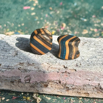 Black and blue double flare ear plugs at 10mm, recycled skateboard layers visible around the profile.