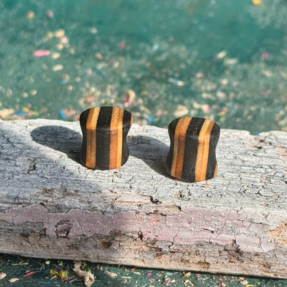 Black Double Flare Wooden Ear Plugs 10mm with striped natural wood design placed on weathered wood surface outdoors