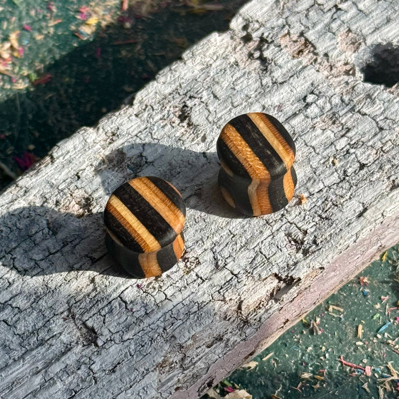 Black Double Flare Wooden Ear Plugs 10mm with striped brown and black wood pattern on rustic surface
