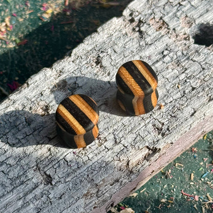 Black Double Flare Wooden Ear Plugs 10mm with striped brown and black wood pattern on rustic surface