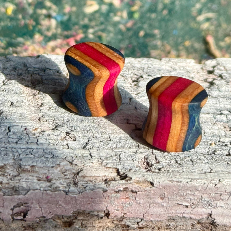 Pink and Blue Double Flare Wooden Ear Plugs 10mm displayed on rustic wood with layered pink, blue, and natural tones.