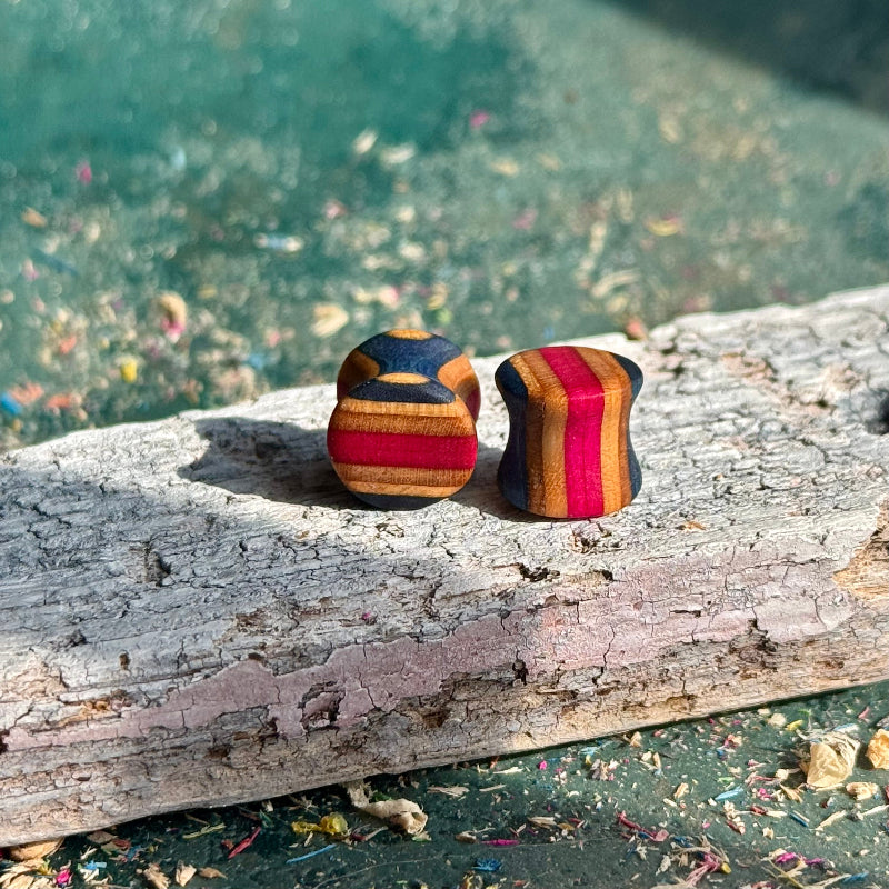 Pink and Blue Double Flare Wooden Ear Plugs 10mm with vibrant striped pattern on a rustic wooden surface.