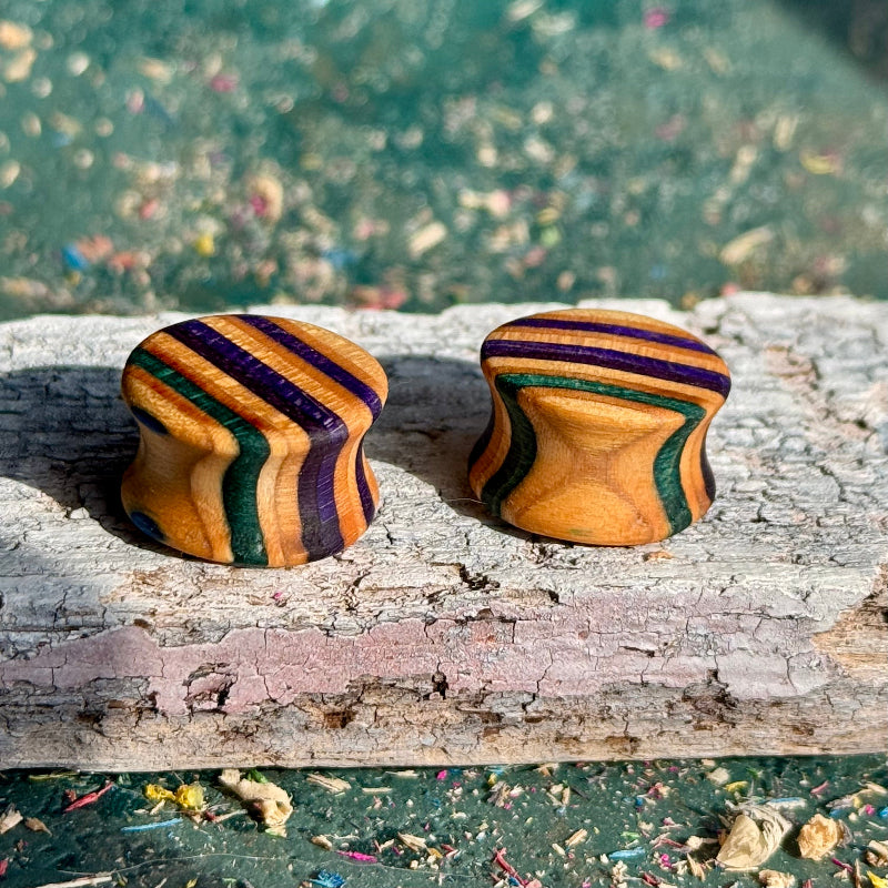 Purple and Teal Double Flare Wooden Ear Plugs 16mm with striped design on weathered wood surface outdoors