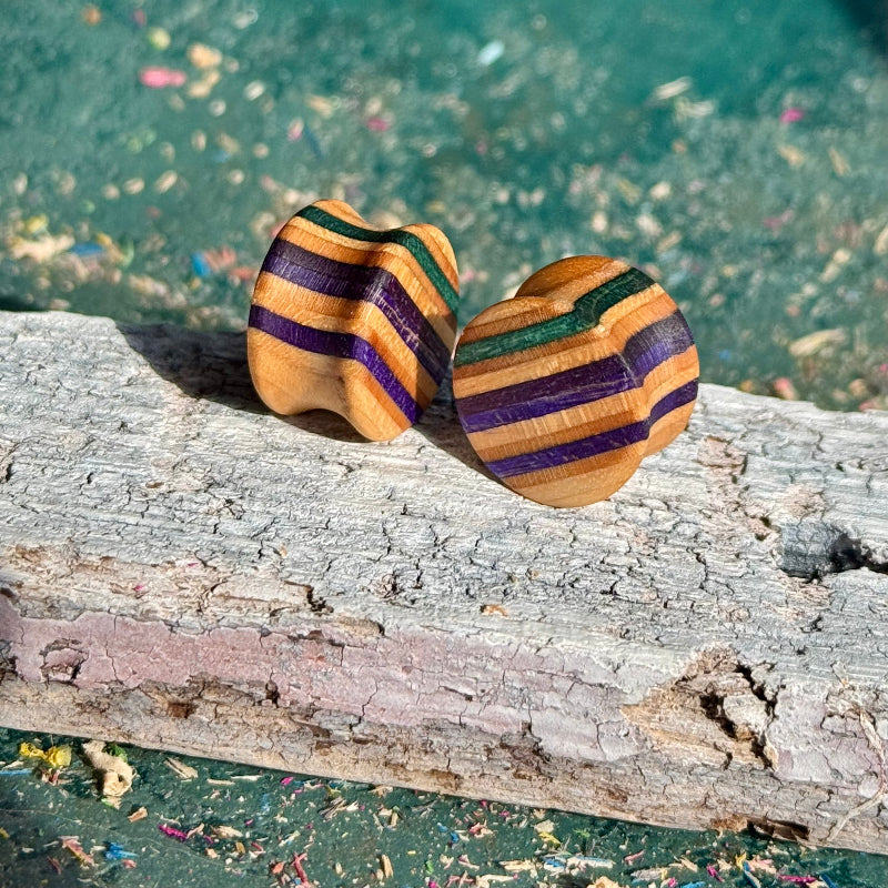 Purple and teal 16mm ear plugs on weathered bark, colour bands running around the profile.