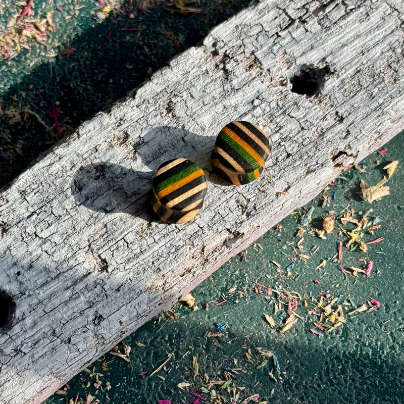 Green, Yellow and Black Double Flare Wooden Ear Plugs 10mm resting on weathered wood with colorful wood shavings nearby