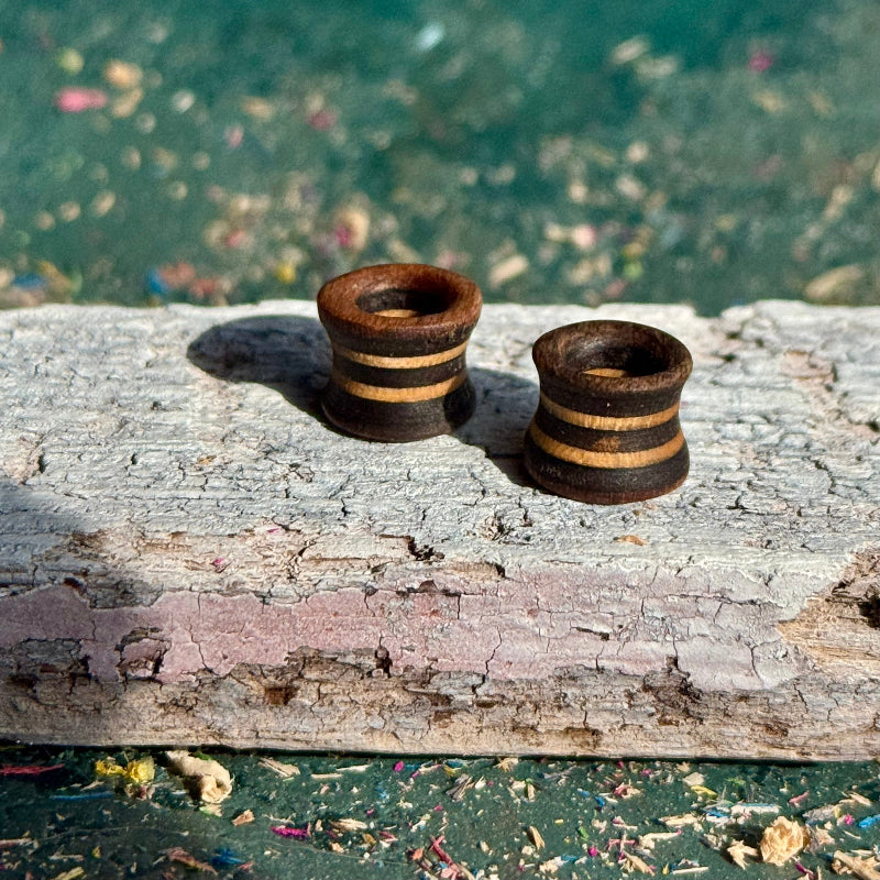 Brown and Grey Flare Wooden Ear Tunnels 10mm with striped design on rustic wooden surface outdoors