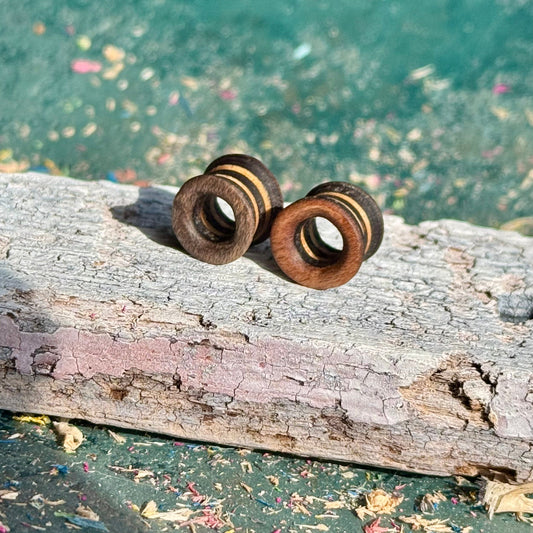 Brown and Grey Flare Wooden Ear Tunnels 10mm placed on weathered wood with blurred blue-green background