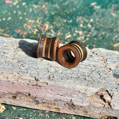 Close-up of handcrafted Brown and Grey Flare Wooden Ear Tunnels 10mm resting on weathered wood surface outdoors