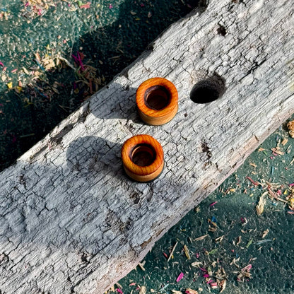 Orange, Purple and Blue Double Flare Wooden Ear Tunnels 10mm resting on a textured piece of weathered wood outdoors
