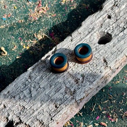 Orange, Purple and Blue Double Flare Wooden Ear Tunnels 10mm placed on weathered wooden surface with scattered wood shavings.