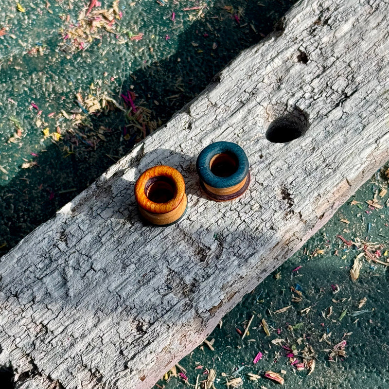 Orange, Purple and Blue Double Flare Wooden Ear Tunnels 10mm resting on weathered wooden surface outdoors with natural sunlight