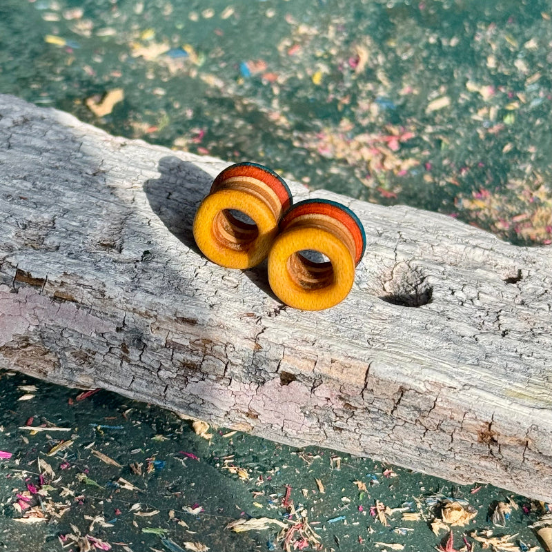 Blue, Orange and Yellow Double Flare Wooden Ear Tunnels 10mm placed on rustic wooden surface outdoors