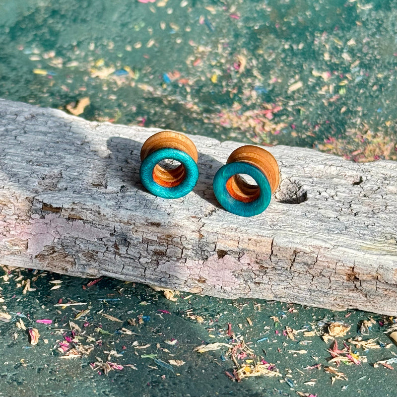 Blue, Orange and Yellow Double Flare Wooden Ear Tunnels 10mm displayed on textured wood surface outdoors
