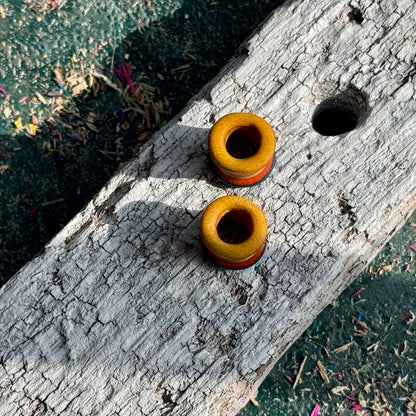 Blue, Orange and Yellow Double Flare Wooden Ear Tunnels 10mm resting on weathered wood under sunlight outdoors
