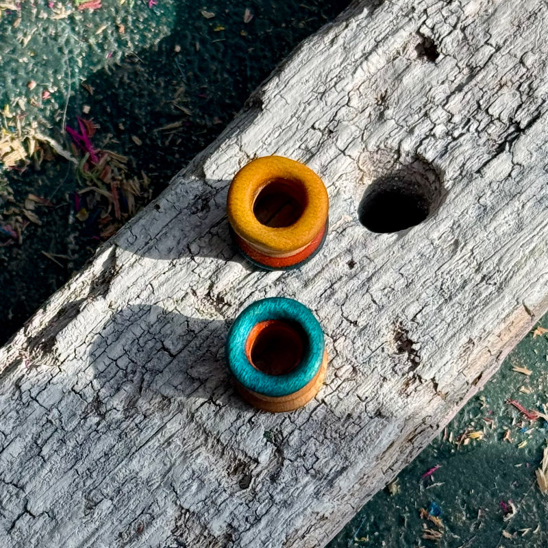 Blue, Orange and Yellow Double Flare Wooden Ear Tunnels 10mm displayed on weathered wooden surface outdoors.