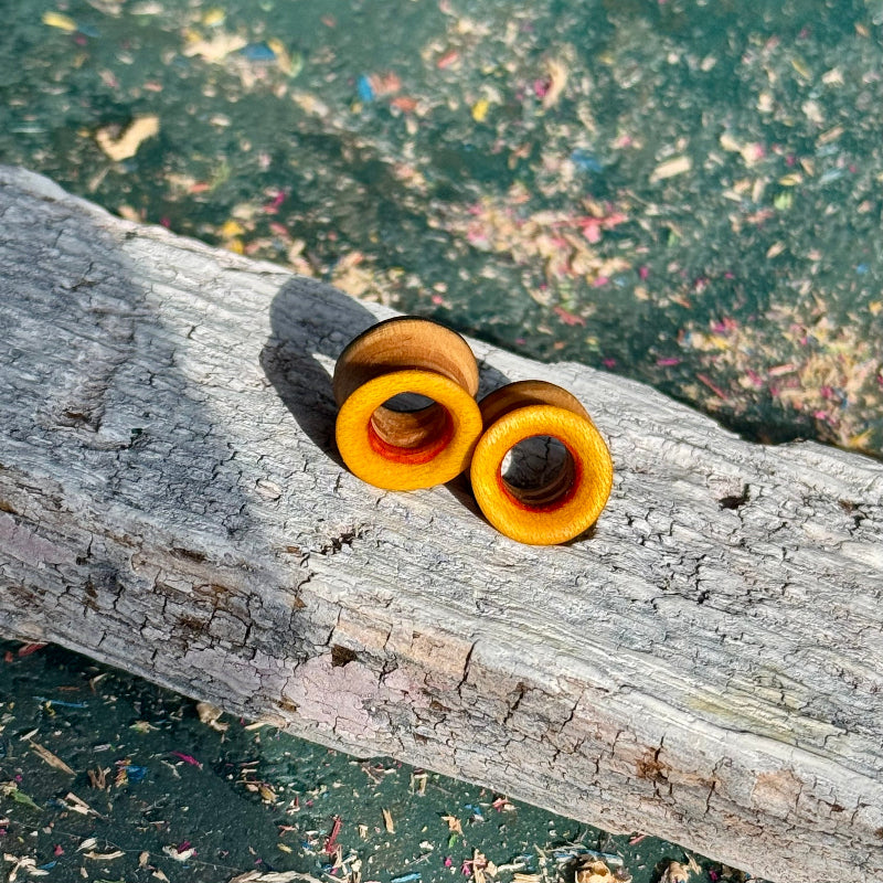 Yellow, Orange and Blue Double Flare Wooden Ear Tunnels 10mm resting on a textured piece of wood outdoors.