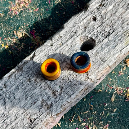 Yellow, Orange and Blue Double Flare Wooden Ear Tunnels 10mm displayed on weathered wood with natural lighting outdoors