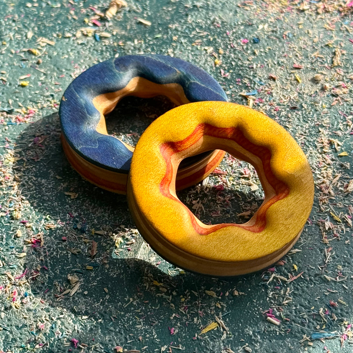 Reversible wooden ear tunnels shown blue side up and yellow side up, with star-shaped carved bores.