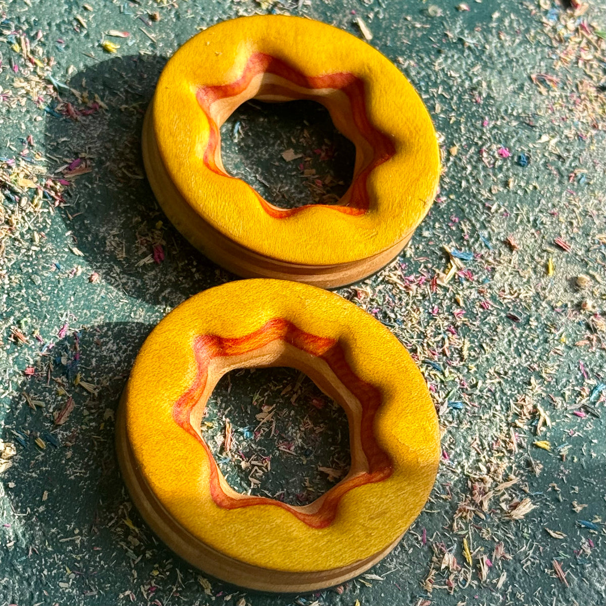 The yellow face of a pair of reversible ear tunnels, orange maple layers exposed around the carved star.