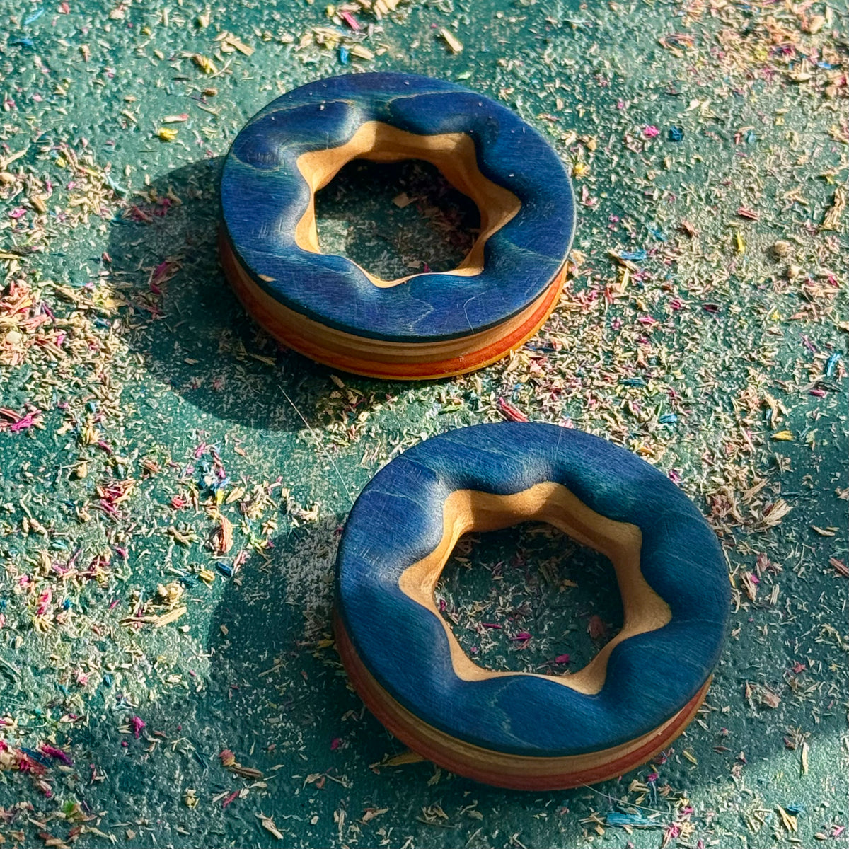 The blue face of a pair of reversible ear tunnels, natural maple showing through the star-shaped bore.