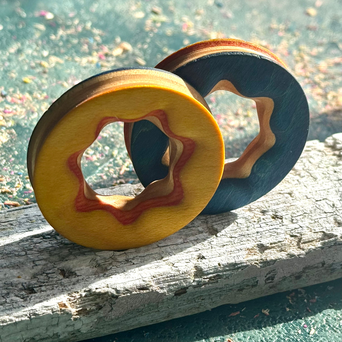 Yellow and blue reversible ear tunnels standing on weathered wood, showing the layered skateboard maple edge.