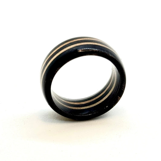 A handcrafted ring made from recycled skateboard wood, featuring sleek black layers with natural wood grain stripes. The ring has a smooth, polished finish and a slightly rounded edge, showcasing the unique layered pattern of the skateboard deck.