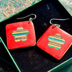 Red recycled skateboard square drop earrings with flower cut-outs, showing green, blue and natural maple colour layers.