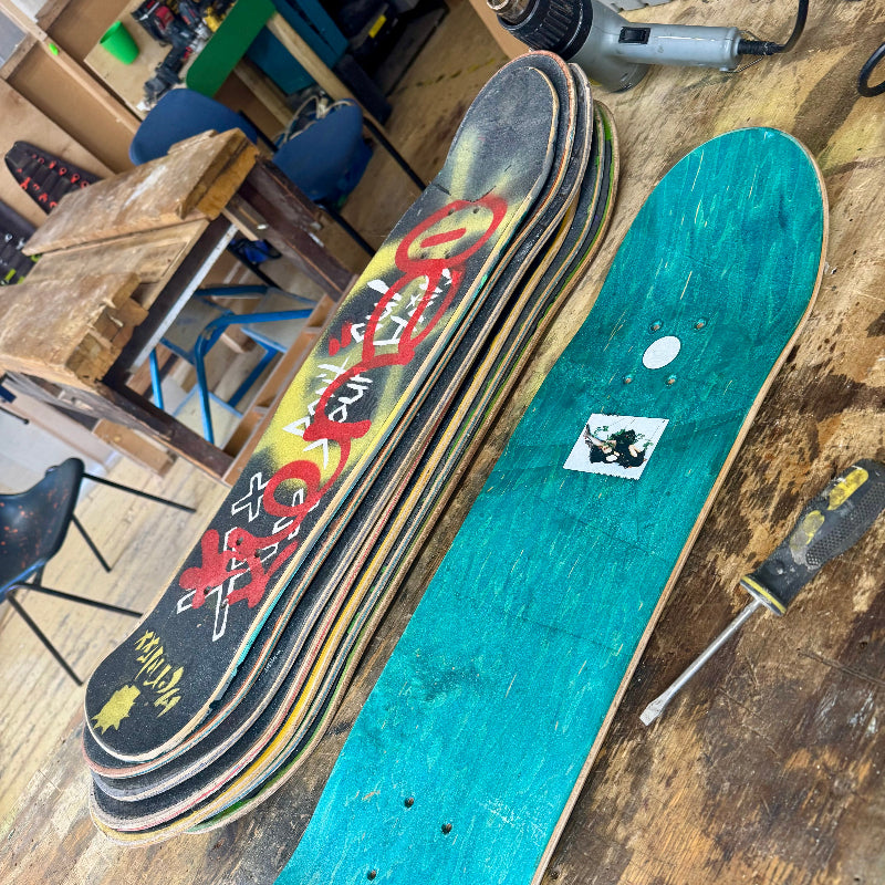 Stack of skateboard decks on a wooden surface with tools in the background