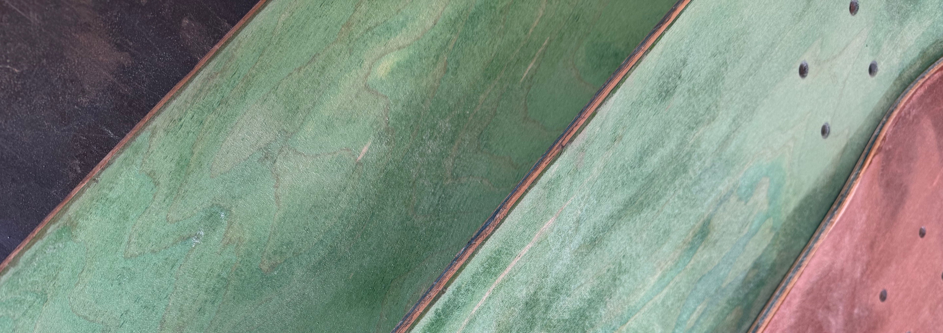 Close-up of a skateboard deck with green and pink coloration.