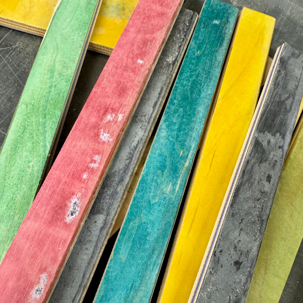 Cut strips of skateboard deck standing on edge, showing green, red, teal, yellow and grey painted faces.