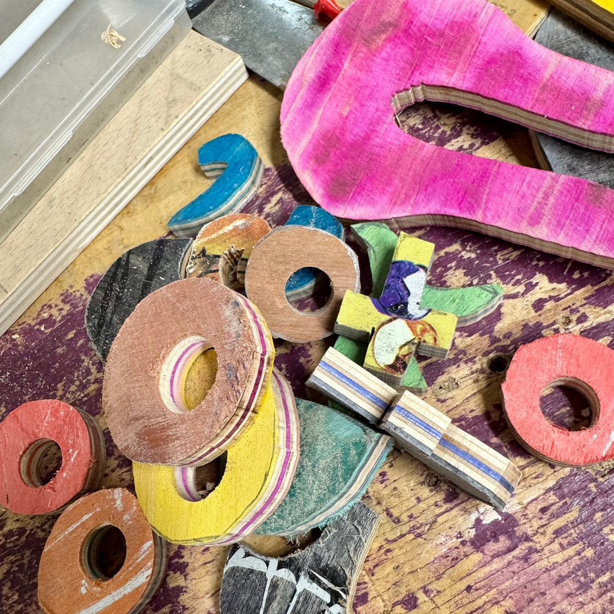 Rough cut ring blanks in red, yellow and brown skateboard maple on a paint marked workbench, with deck offcuts and a pink deck nose.
