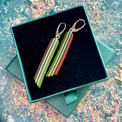 Wooden earrings with striped design in a black box on a textured surface