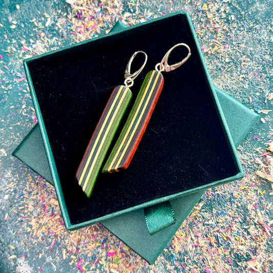 Wooden earrings with striped design in a black box on a textured surface