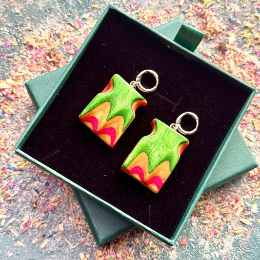 Colorful earrings in a green box on a textured surface