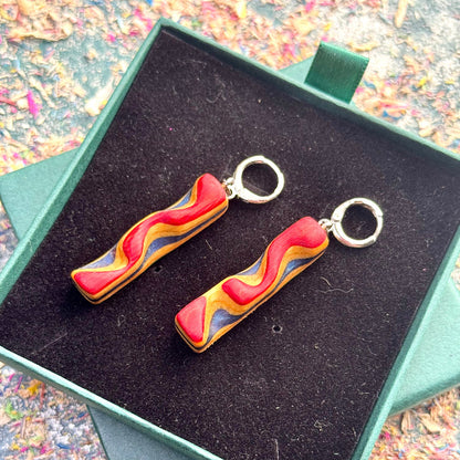 Colorful wavy earrings on a black cushion in a green box with a multicolored background