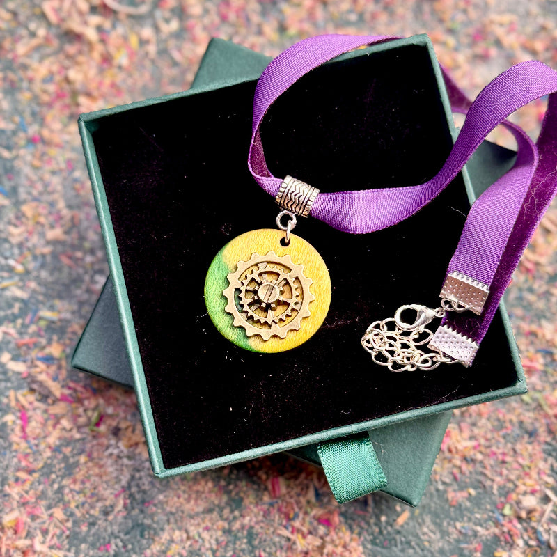 Yellow gear choker with a circular maple pendant and brass gear detail on a purple ribbon.