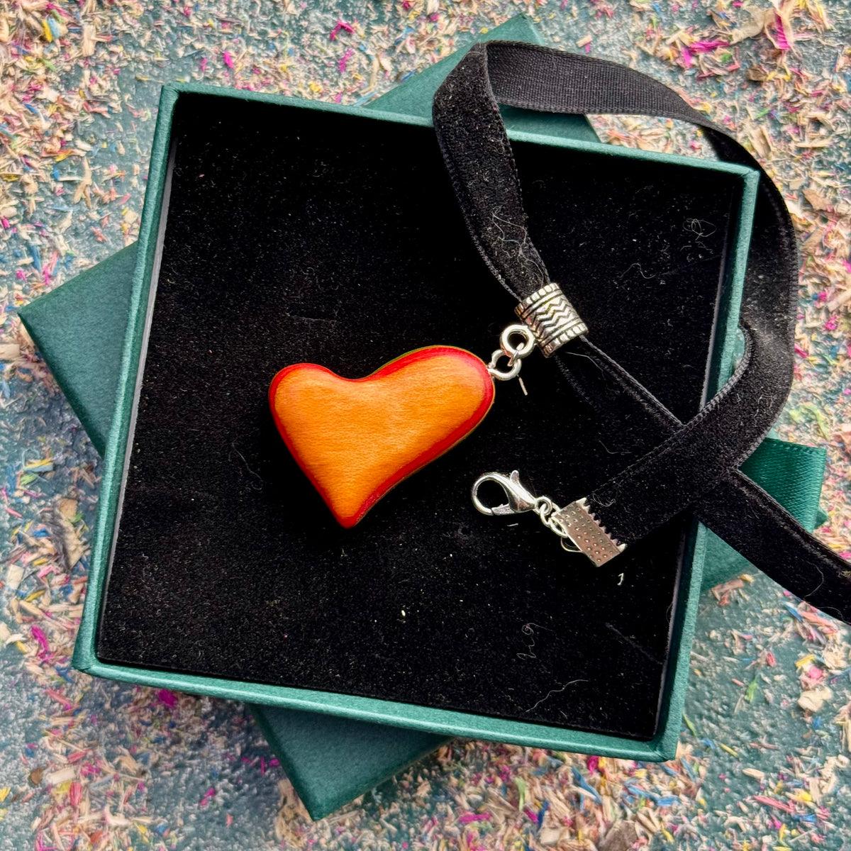 Orange heart choker pendant in skateboard maple on a black velvet strap, in an open gift box.